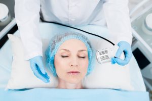 Contemporary beautician using electric device for cleansing skin of client